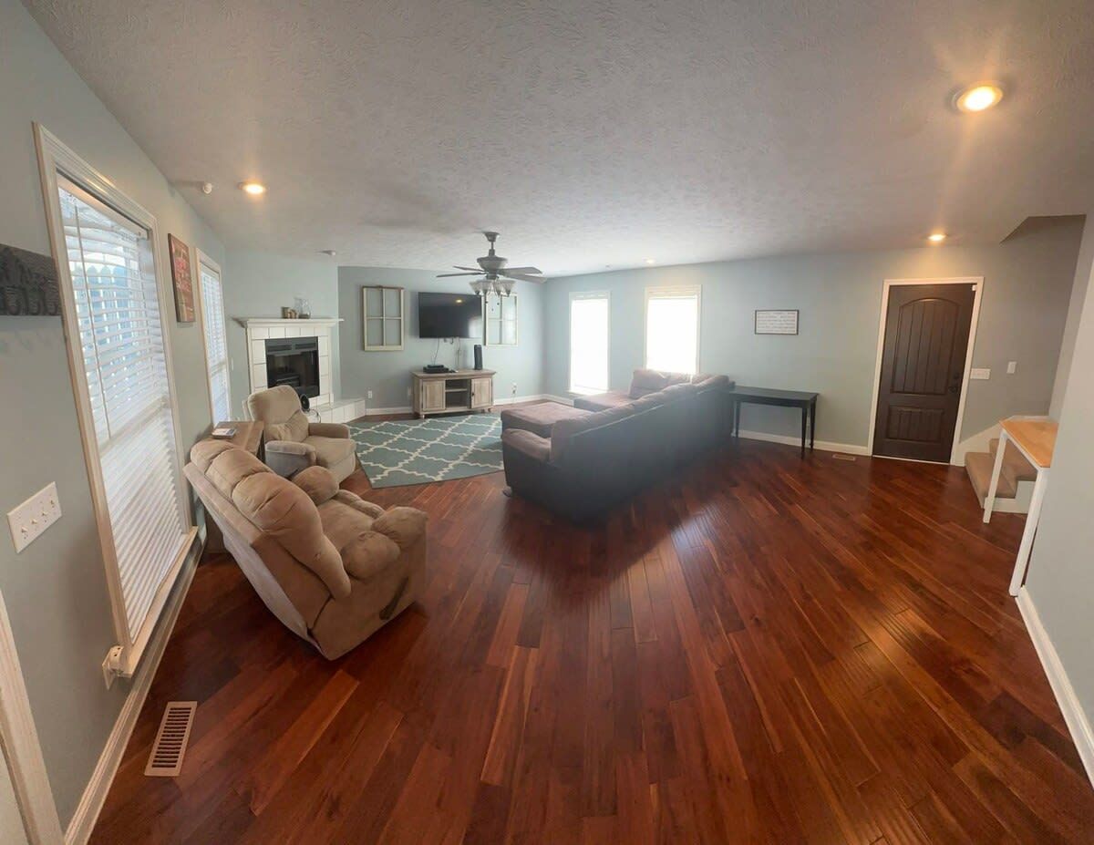 Un ampio soggiorno con parquet, una ventola a soffitto e un camino.