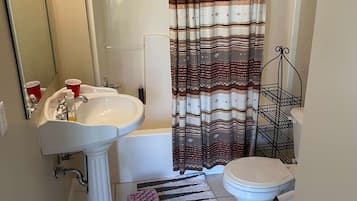 A bathroom with a shower, toilet, sink, and a striped rug.