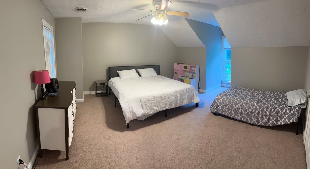 A bedroom with a bed, a desk, a chair, and a ceiling fan.