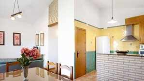 Ein Essbereich mit Tisch, Stühlen, einer Blumenvase und einer Küche mit Backsteinwand und Holzschränken.