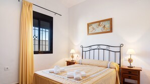 Ein ordentlich bezogenes Bett mit Handtüchern, ein Fenster mit Vorhängen, ein Bild an der Wand und zwei Nachttische mit Lampen.