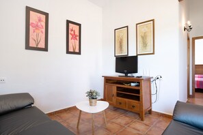 Una stanza con un divano, un tavolino con una pianta, una televisione su un mobile in legno e opere d'arte alle pareti.
