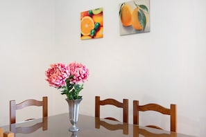 Un tavolo da pranzo con un vaso di fiori, sedie di legno e due dipinti di frutta appesi al muro.