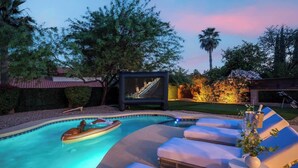 A pool area with lounge chairs, a hot tub, and a television screen. - Sleeps 18 | Beautiful Resort Style | Heated Pool (Scottsdale)