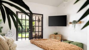 A bedroom with a large bed, a flat-screen TV mounted on the wall, a wooden cabinet, and a green ottoman. - Sleeps 18 | Beautiful Resort Style | Heated Pool (Scottsdale)