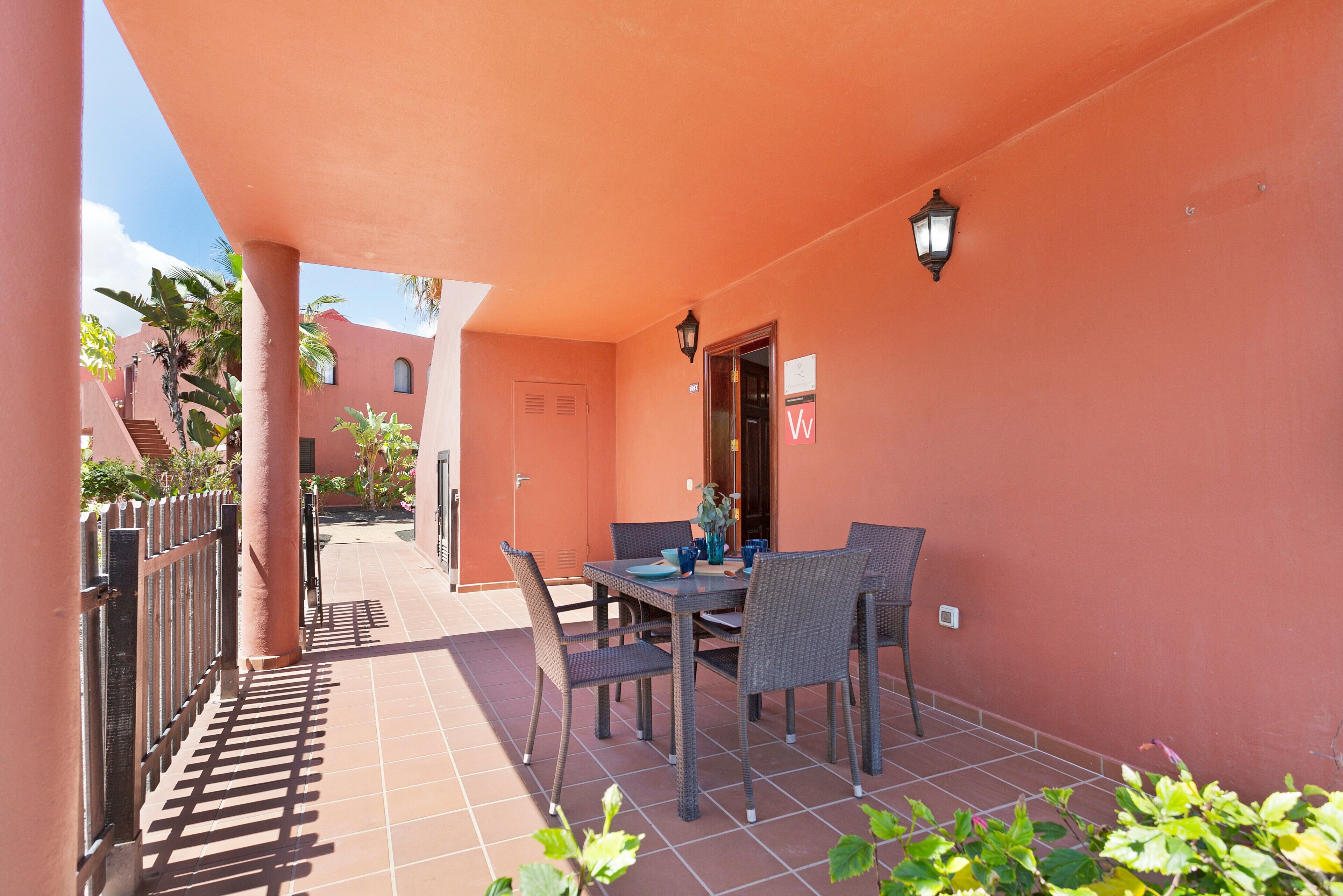 A covered outdoor patio with a table and chairs, a door, and a wall-mounted light fixture.