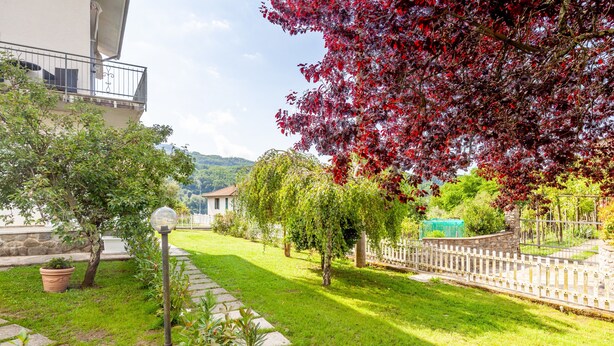 A well-maintained garden with a stone pathway, a lamp post, and a variety of trees including one with red leaves. - Villa La Lanterna Bianca Apartment with Mountain View, Wi-Fi, and Air Conditioning (Bagnone)