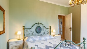 A bedroom with a bed, two bedside tables, a nightstand, a chandelier, and a door leading to another room. - Villa La Lanterna Bianca Apartment with Mountain View, Wi-Fi, and Air Conditioning (Bagnone)