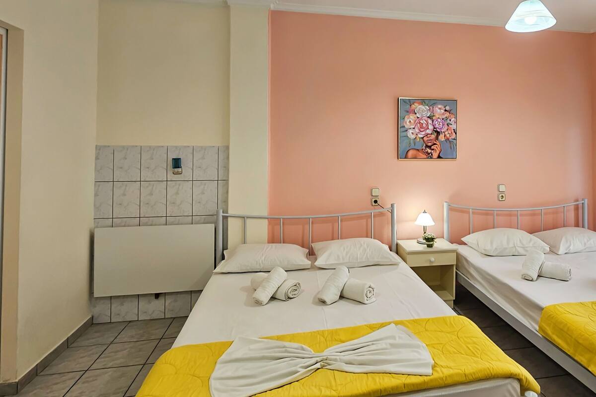 A hotel room with two beds, each with white linens and towels, a painting on the wall, and a window with sheer curtains.