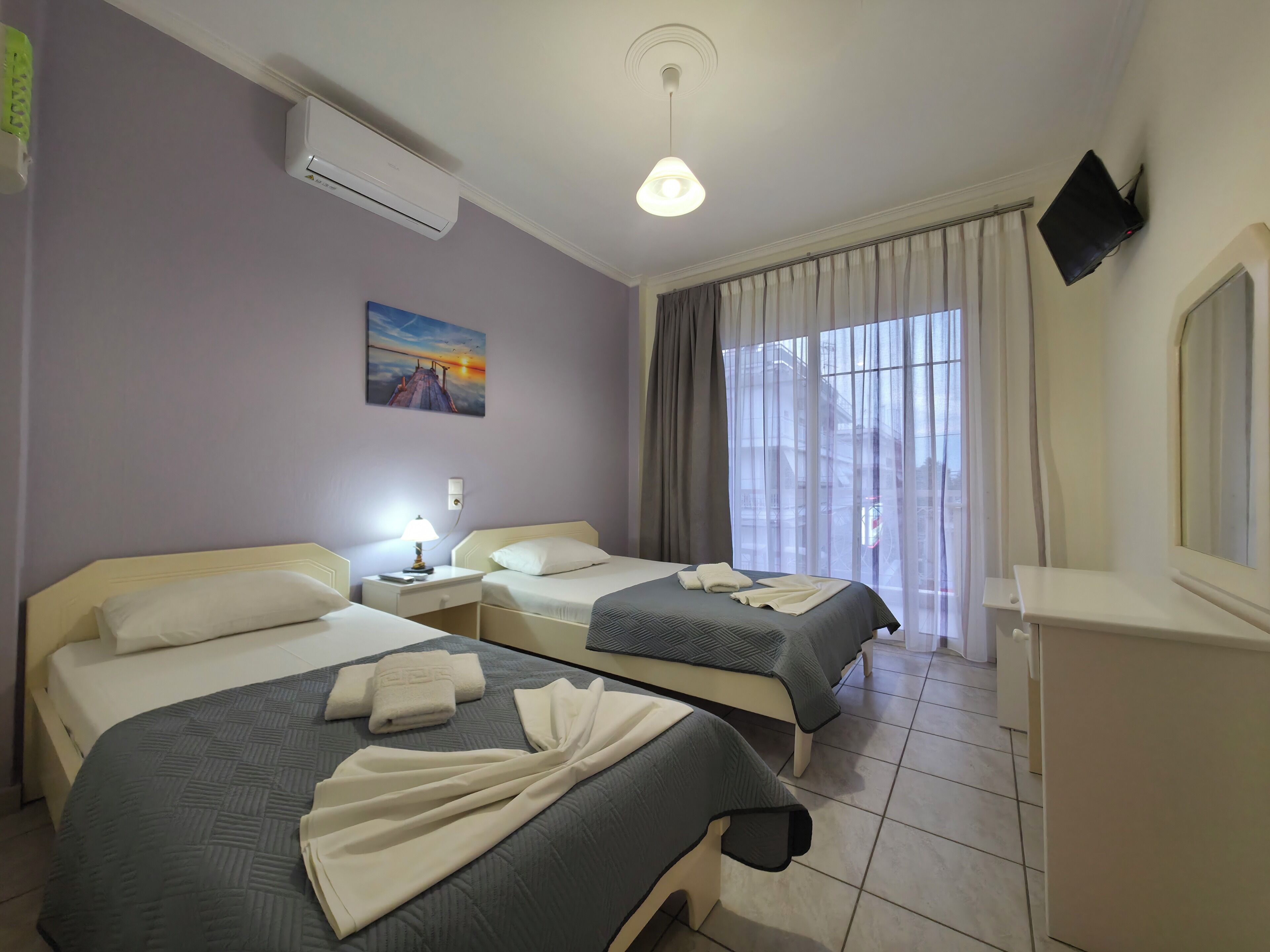 Ein Hotelzimmer mit zwei Betten, einem Gemälde, einem Fernseher und einem Fenster mit Vorhängen.