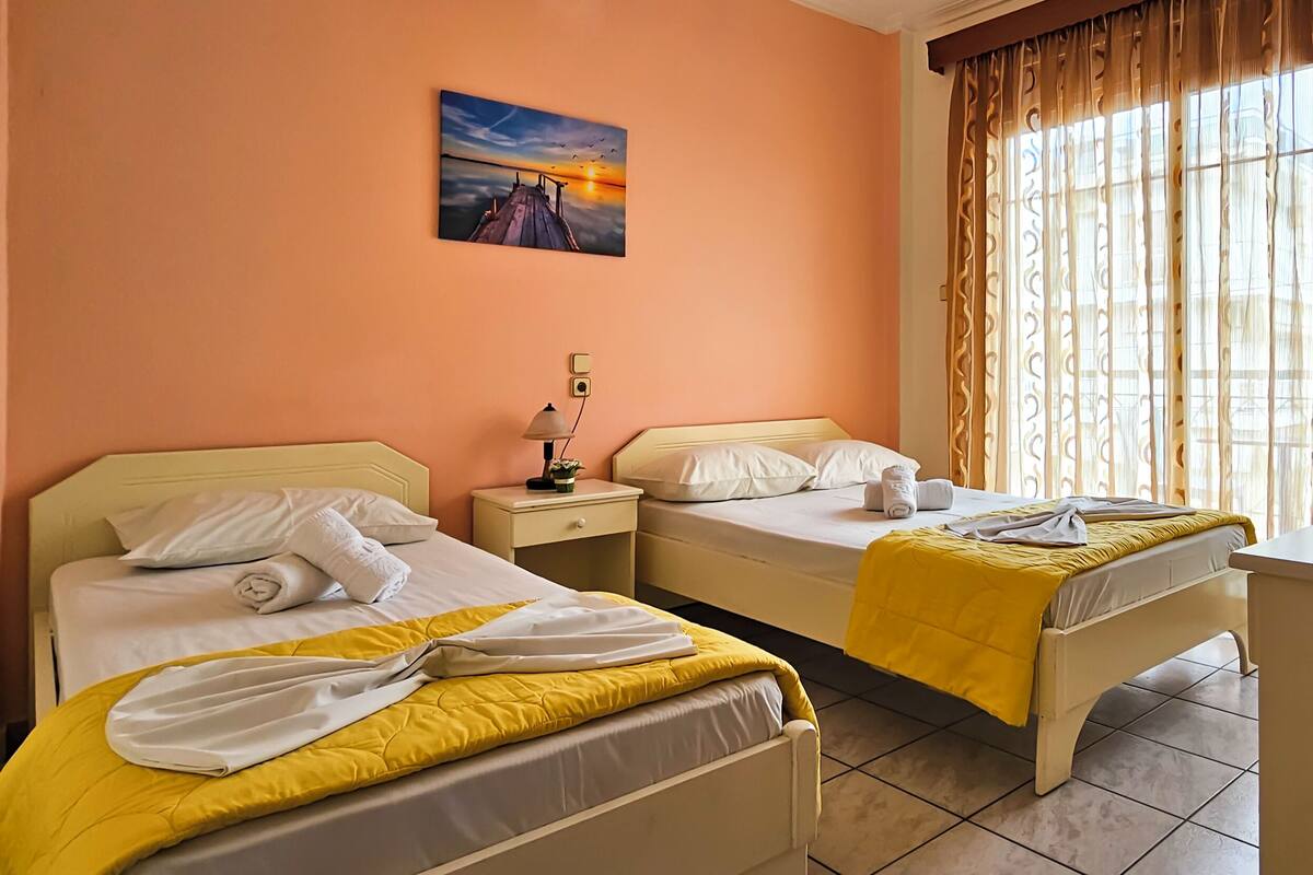 A hotel room with two beds, a painting on the wall, and a window with curtains.