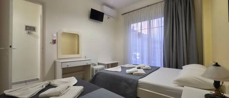 Une chambre d’hôtel avec deux lits, un bureau avec un miroir, un téléviseur à écran plat, une fenêtre avec des rideaux et une télécommande sur la table de chevet.