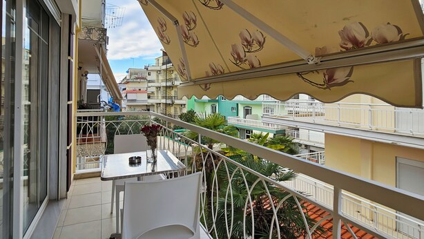 A balcony with a table and chairs, a flower vase, and a view of neighboring buildings. - Chariclia Hotel (Katerini)