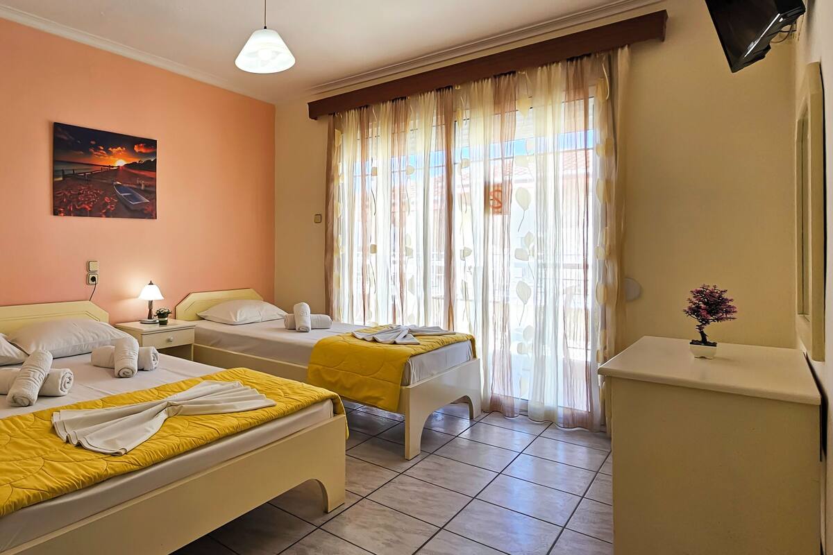 A hotel room with two beds, a painting on the wall, a TV mounted on the wall, and a window with curtains.