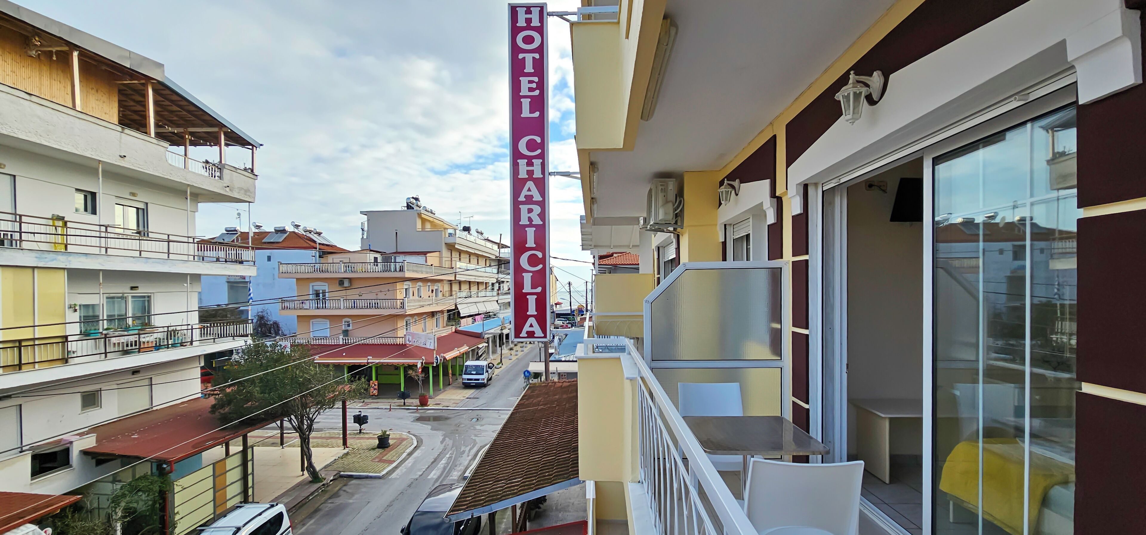 A hotel named 'HOTEL CHARICIA' with a balcony overlooking a street with other buildings.