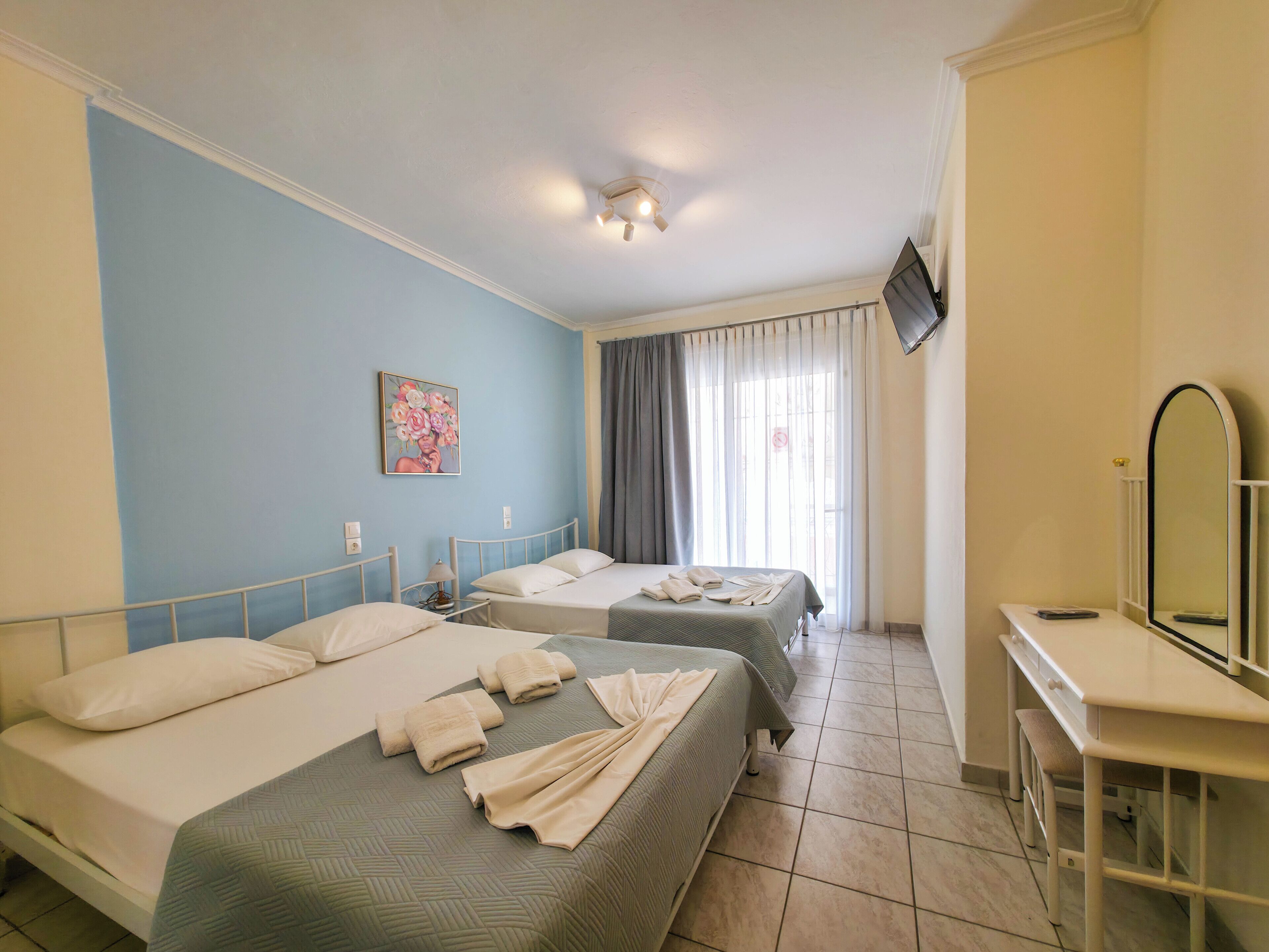 Ein Hotelzimmer mit zwei Betten, einem Schreibtisch, einem Fernseher und einem Bild an der Wand.