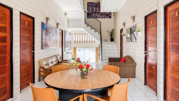 Uma sala espaçosa com uma mesa redonda de madeira, cadeiras de vime, um sofá e uma escada que leva a um andar superior.