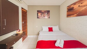 Quarto de hotel com cama, guarda-roupa de madeira, escrivaninha e cadeira, e um quadro na parede.