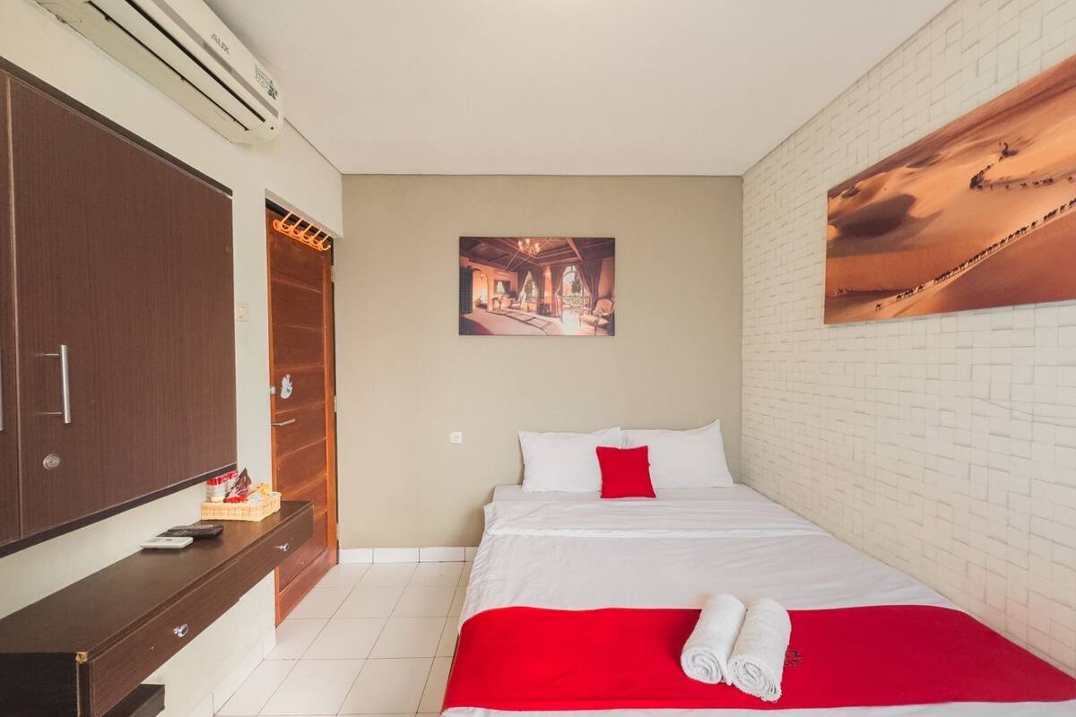 Une chambre d’hôtel avec un lit, une armoire en bois, un bureau avec une chaise et un tableau au mur.