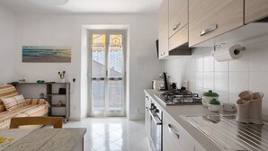 A modern kitchen with white cabinets, a gas stove, and a dining area with a table and chairs. - Apartment 'Da Ercolino' with Sea View, Balcony and Wi-Fi (Pitelli)