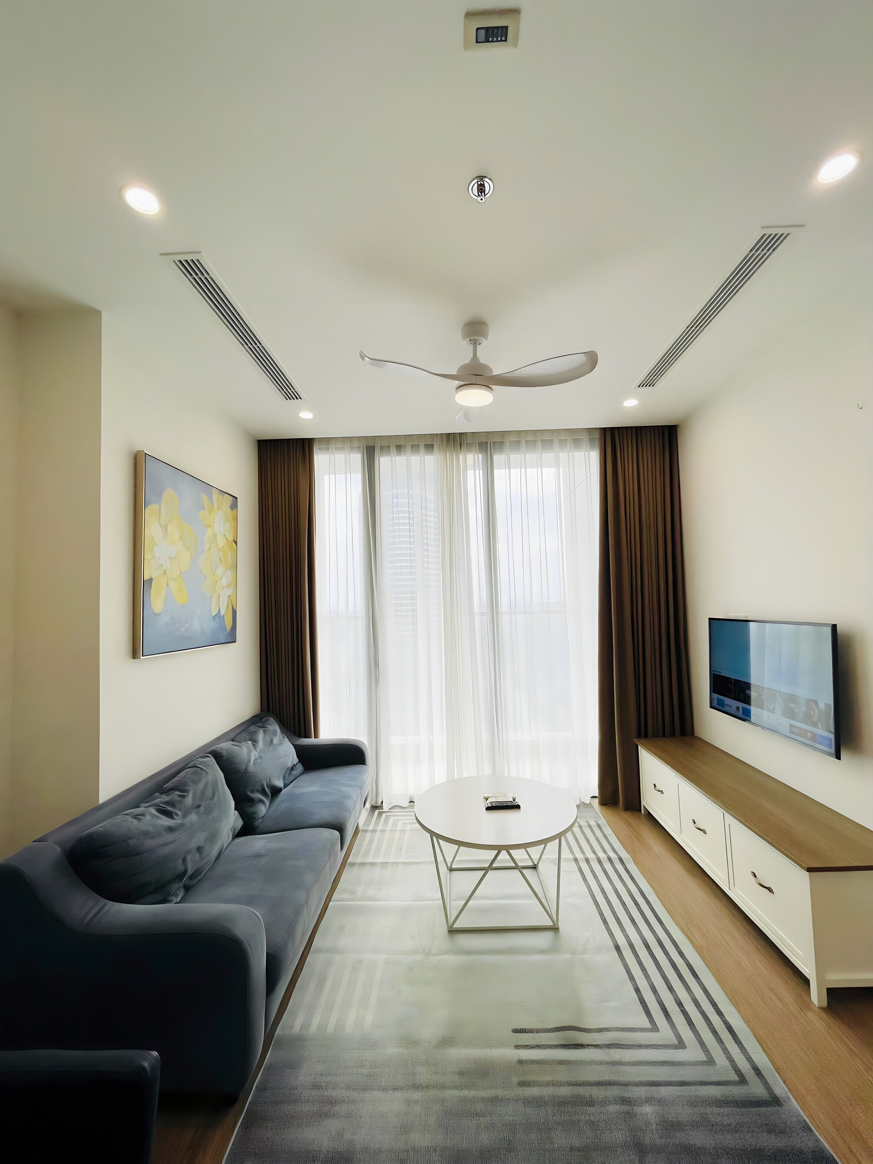 A modern living room with a sofa, a coffee table, a TV, and a ceiling fan.