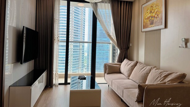 A modern living room with a sofa, a coffee table, a TV mounted on the wall, and a large window offering a city view. - Mira Housing- Vinhome Skylake Luxury Apartment  (Hanoi)