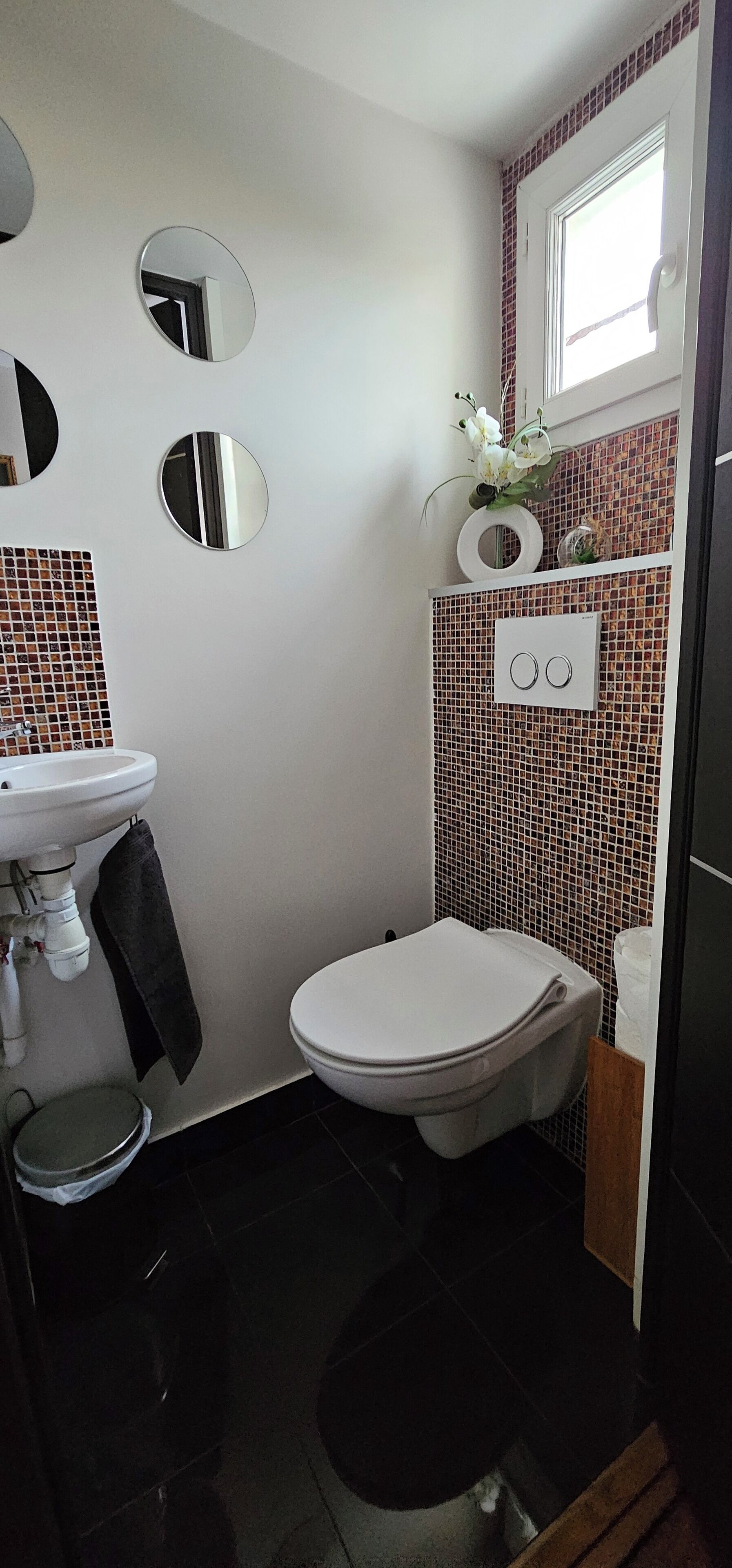 A compact bathroom with a white sink, a toilet, and a small trash bin.