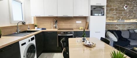 Una cocina compacta con lavadora, una mesa de comedor y un muro de piedra.