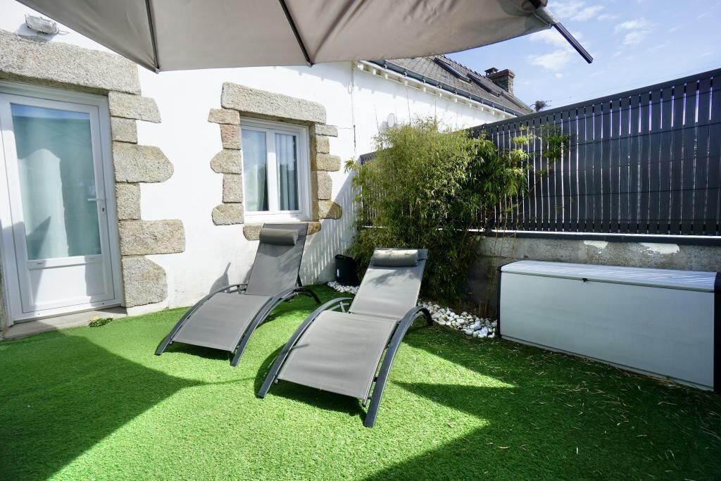 A patio with two reclining chairs under a canopy, a white building with stone accents, and a black fence.