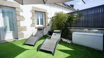 A patio with two reclining chairs under a canopy, a white building with stone accents, and a black fence.