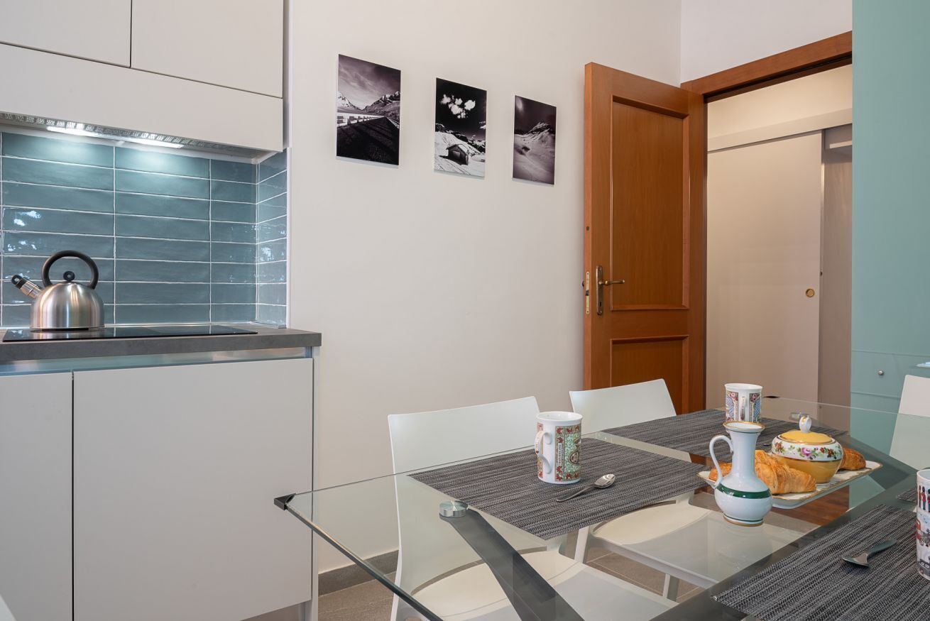 Une cuisine moderne équipée d’une bouilloire, d’une table à manger avec des chaises et d’une porte donnant sur une autre pièce.