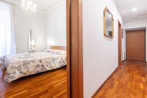 A bedroom with a bed, a chandelier, a mirror, and a wooden floor.