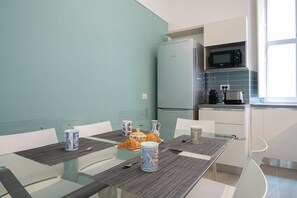 A modern kitchen with a refrigerator, microwave, and coffee maker. There is a dining table with chairs and a breakfast setup.