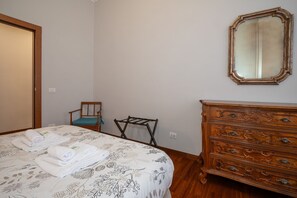 A bedroom with a bed, a wooden dresser, a chair, and a mirror.