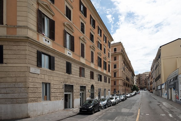 Una calle con coches aparcados y edificios con numerosas ventanas y puertas.