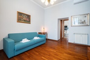 A room with a blue sofa, a painting on the wall, a radiator, and a door leading to another room.