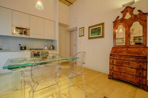 A modern kitchen with a glass dining table and chairs, a wooden dresser, and framed artwork on the wall. - Gracchi Apartment Prati (Roma)