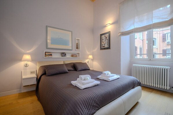A bedroom with a bed, two bedside lamps, a window with a view, and a radiator.