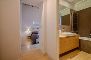 A modern bathroom with a large mirror, a bathtub, and a wooden vanity.