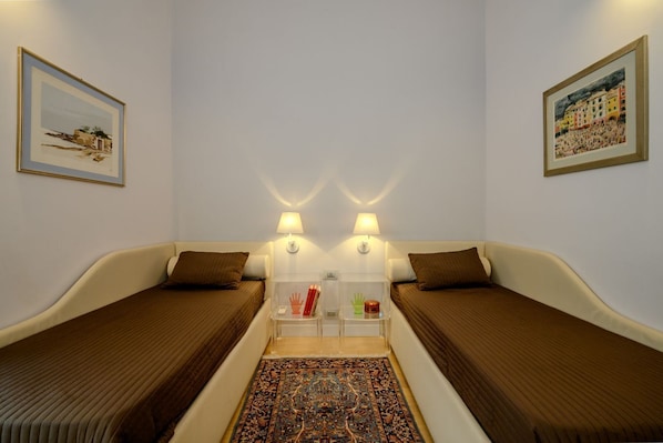 Una habitación con dos camas, un tapete, obras de arte en la pared y lámparas de noche.