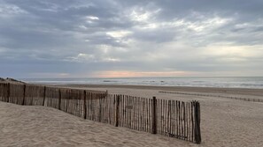 A sandy beach with a wooden fence and the ocean in the background.