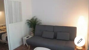 A room with a grey sofa, a small white side table, a potted plant, and a lamp. - Petit Cocon a 150m de L'océan (Soulac-sur-Mer)
