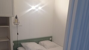 A small, single-bed room with a green headboard, a bedside lamp, and a white wall. - Petit Cocon a 150m de L'océan (Soulac-sur-Mer)