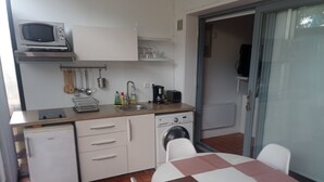 A compact kitchen with a microwave, sink, and small refrigerator. There is a table with chairs and a glass door leading to a balcony. - Petit Cocon a 150m de L'océan (Soulac-sur-Mer)
