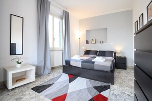 A bedroom with a bed, bedside tables, a nightstand, a dresser, a mirror, a window with curtains, and a patterned rug. - Opera 65 Roof Terrace (Roma)