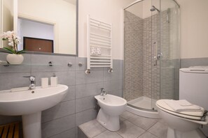 A modern bathroom with a sink, bidet, toilet, and glass shower enclosure.