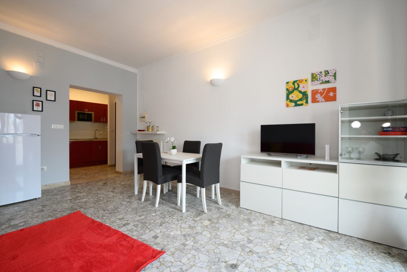 Una cucina moderna con mobili bianchi, un'area pranzo con tavolo e sedie, una TV e opere d'arte alle pareti.