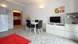 Une cuisine moderne avec des meubles blancs, un coin repas comprenant une table et des chaises, un téléviseur et des œuvres d’art accrochées au mur.