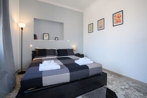 A modern hotel room with a large bed, bedside tables, a floor lamp, and artwork on the walls.
