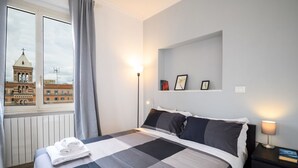 Une chambre d’hôtel avec un lit, une table de chevet, une lampe, une fenêtre avec des rideaux et une vue sur un immeuble doté d’une tour.